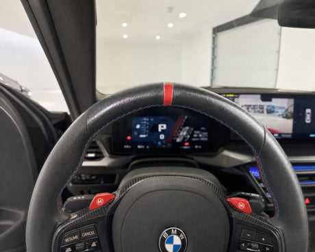 Speckig glänzendes Lederlenkrad eines weißen BMW M2 im Cockpit, der Fettglanz an der Zehn-Uhr-Position hebt sich von der matt